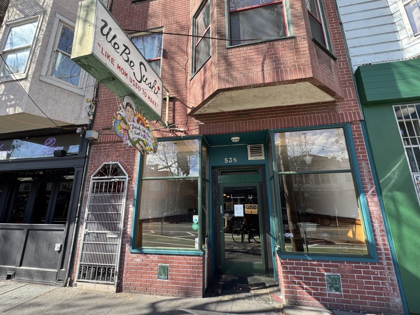 Street view of the entrance to U & I Sushi restaurant with a green-framed door and windows, a hanging sign, and a "closed" sign on the door.