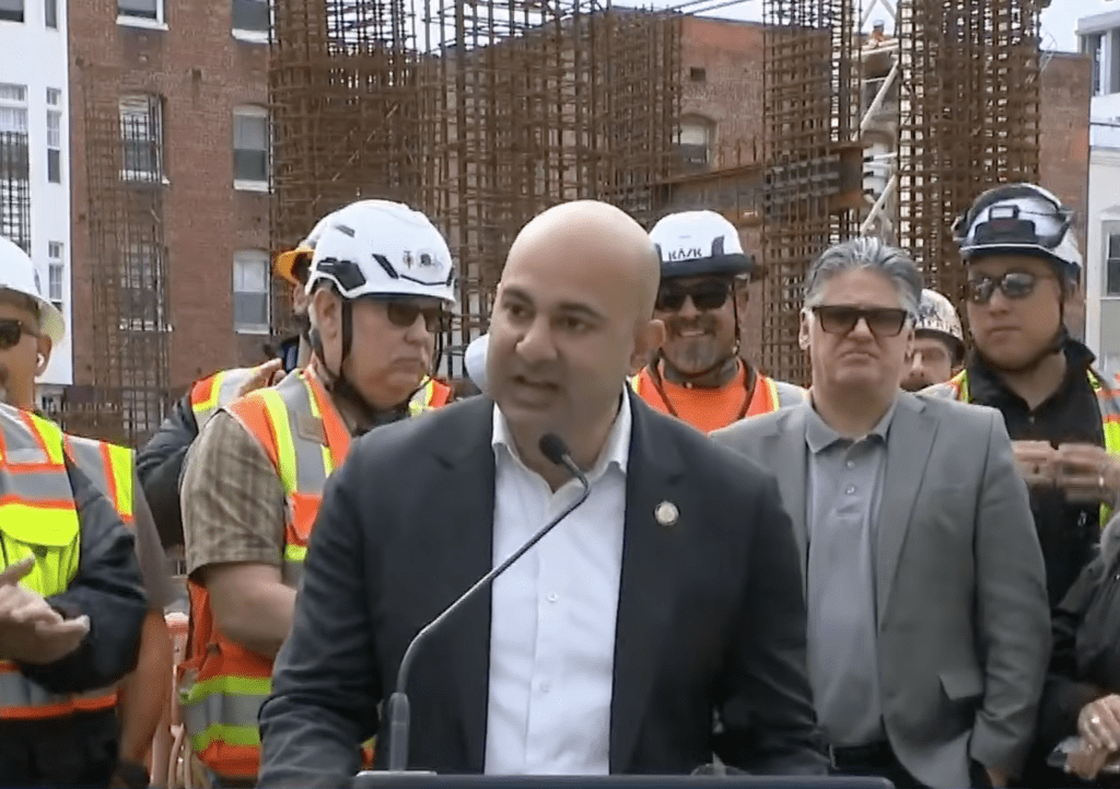 District 5 Supervisor Bilal Mahmood speaks at a press conference with construction workers in the background.