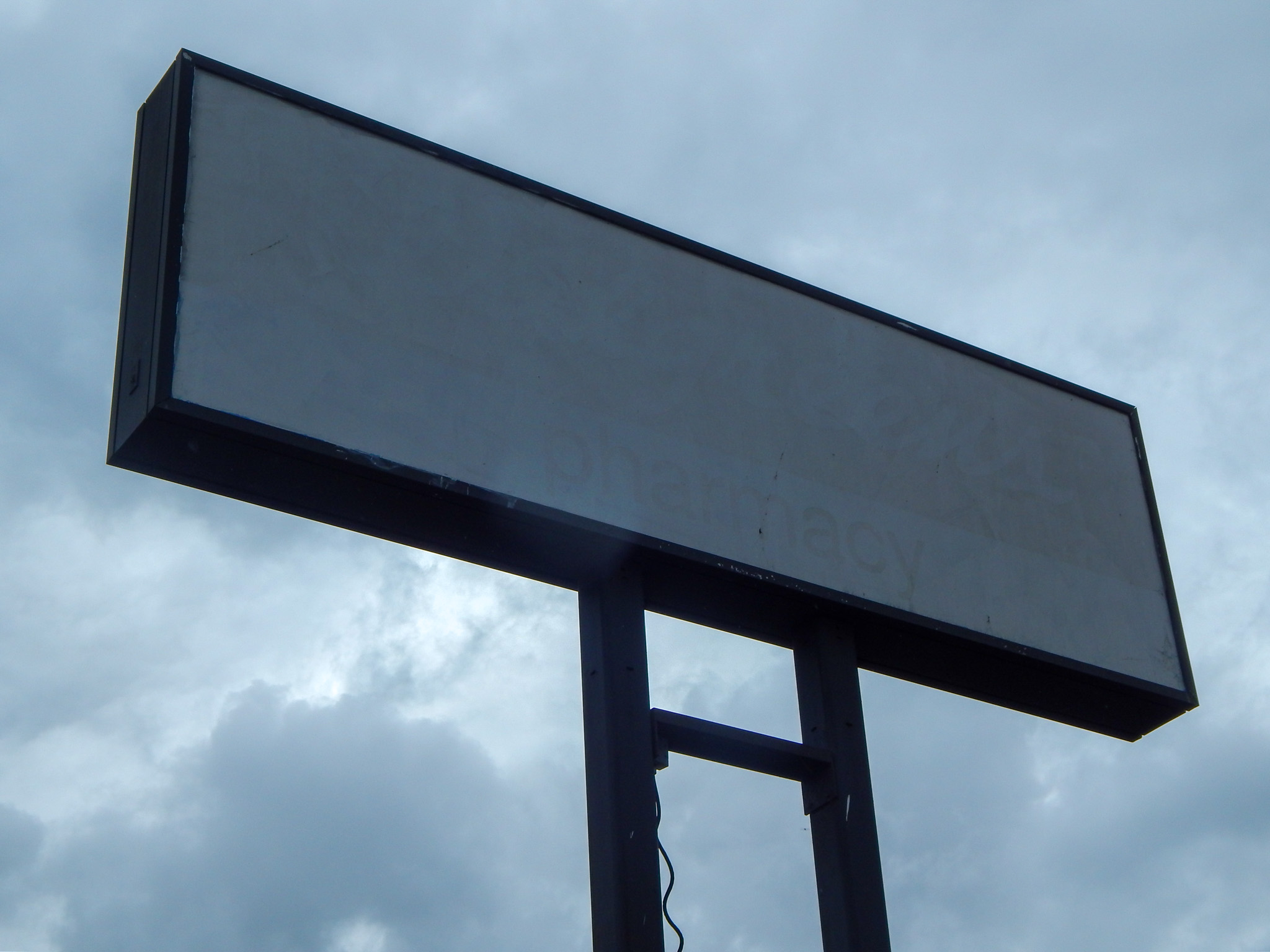 A blank, rectangular outdoor sign mounted on two metal poles stands against a cloudy sky.