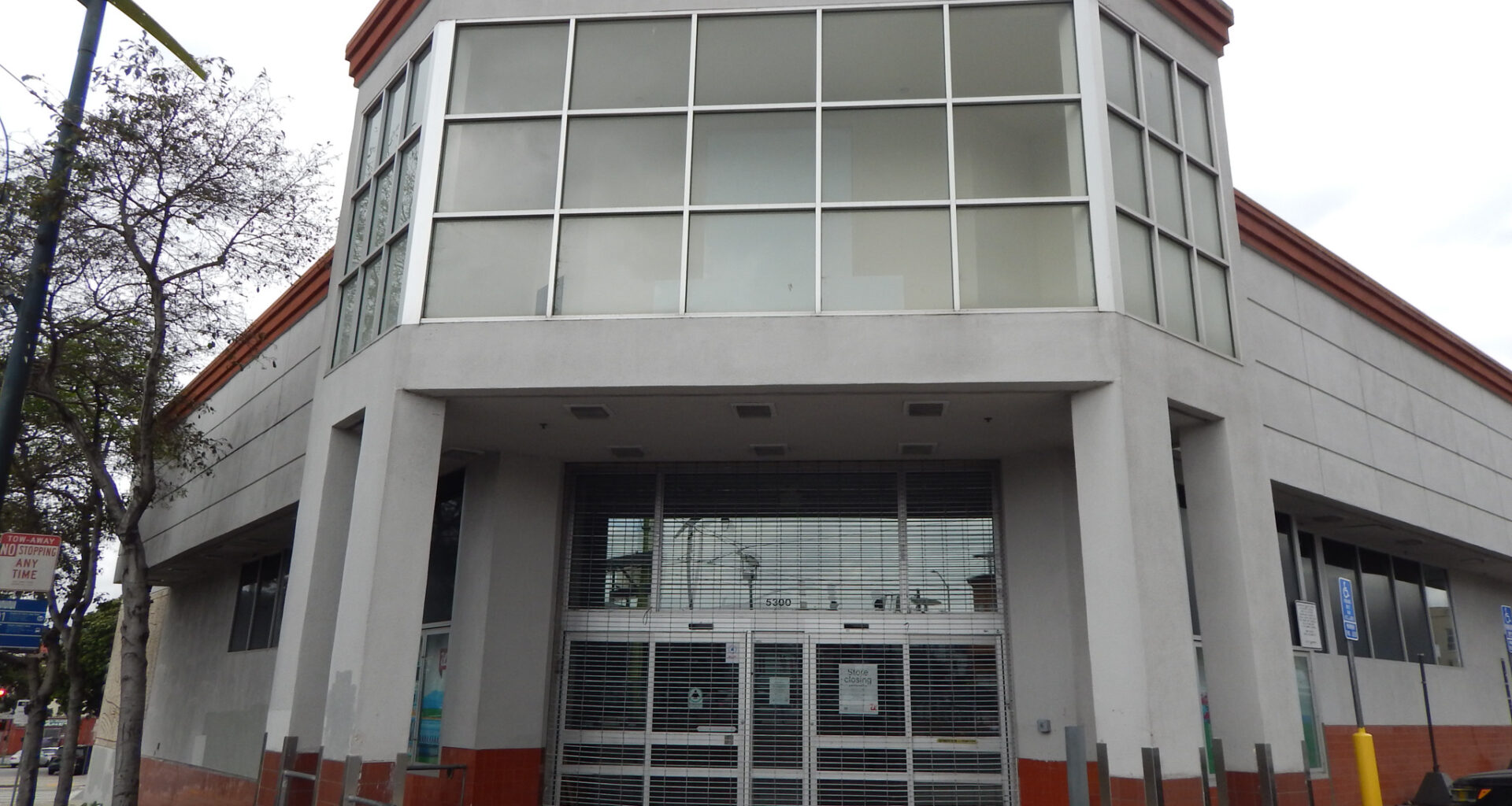 A two-story, gray and red commercial building with large windows and a closed metal security gate over the entrance.