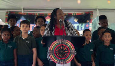 adult female standing on a stage with several elementary age children