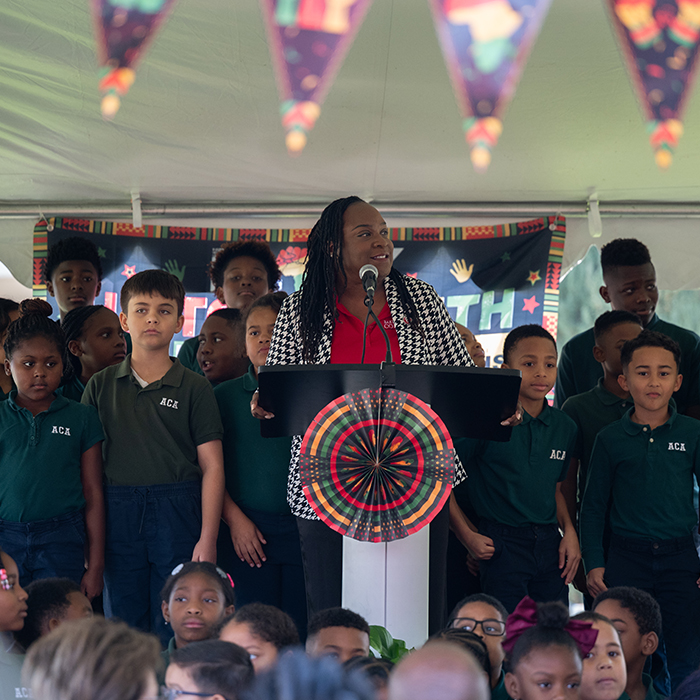 adult female standing on a stage with several elementary age children