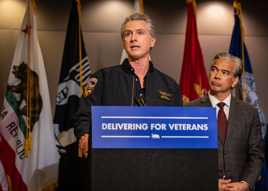 California Governor Gavin Newsom at a podium with "Delivering for Veterans" on the front, next to Attorney General Rob Bonta.