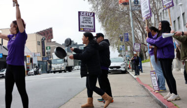 A group of people on a city sidewalk hold SEIU strike signs and bang pots, protesting unfair labor practices.
