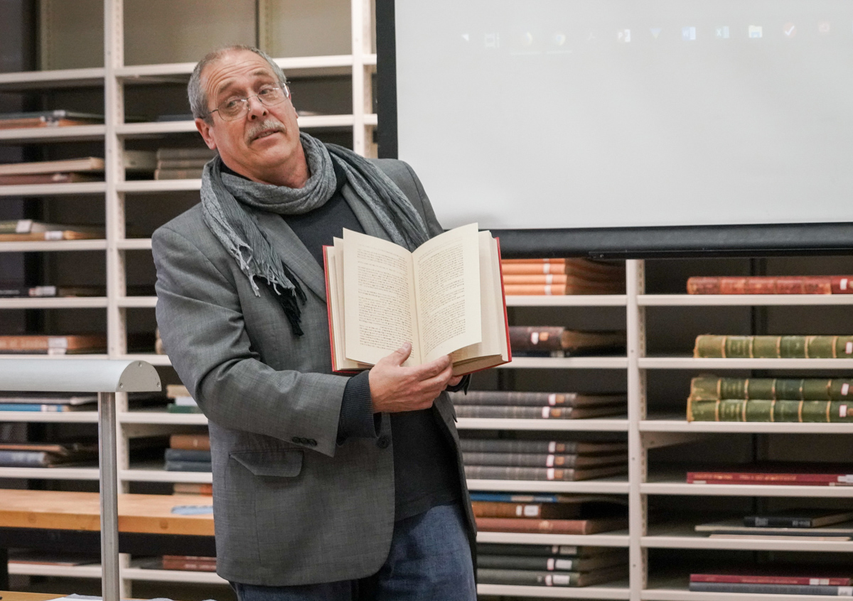 David Eifler holds up a book in front of a wall storing larger books
