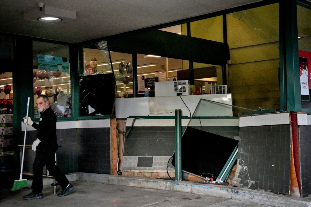 An employee sweeps broken glass in front of a Safeway grocery store after a vehicle crashed into the entrance.