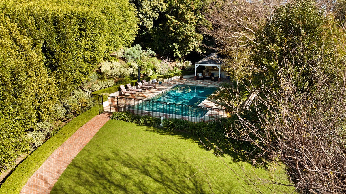 The backyard features manicured lawns and a swimming pool with a cabana.