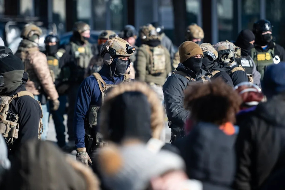 Federal agents stand guard against a growing wall of protesters on Jan. 24 in Minneapolis.
