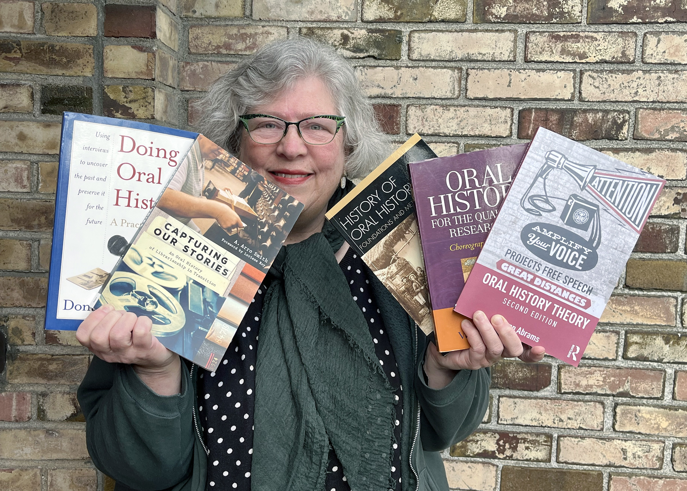 Librarian Ann Glusker holds an array of books and smiles 