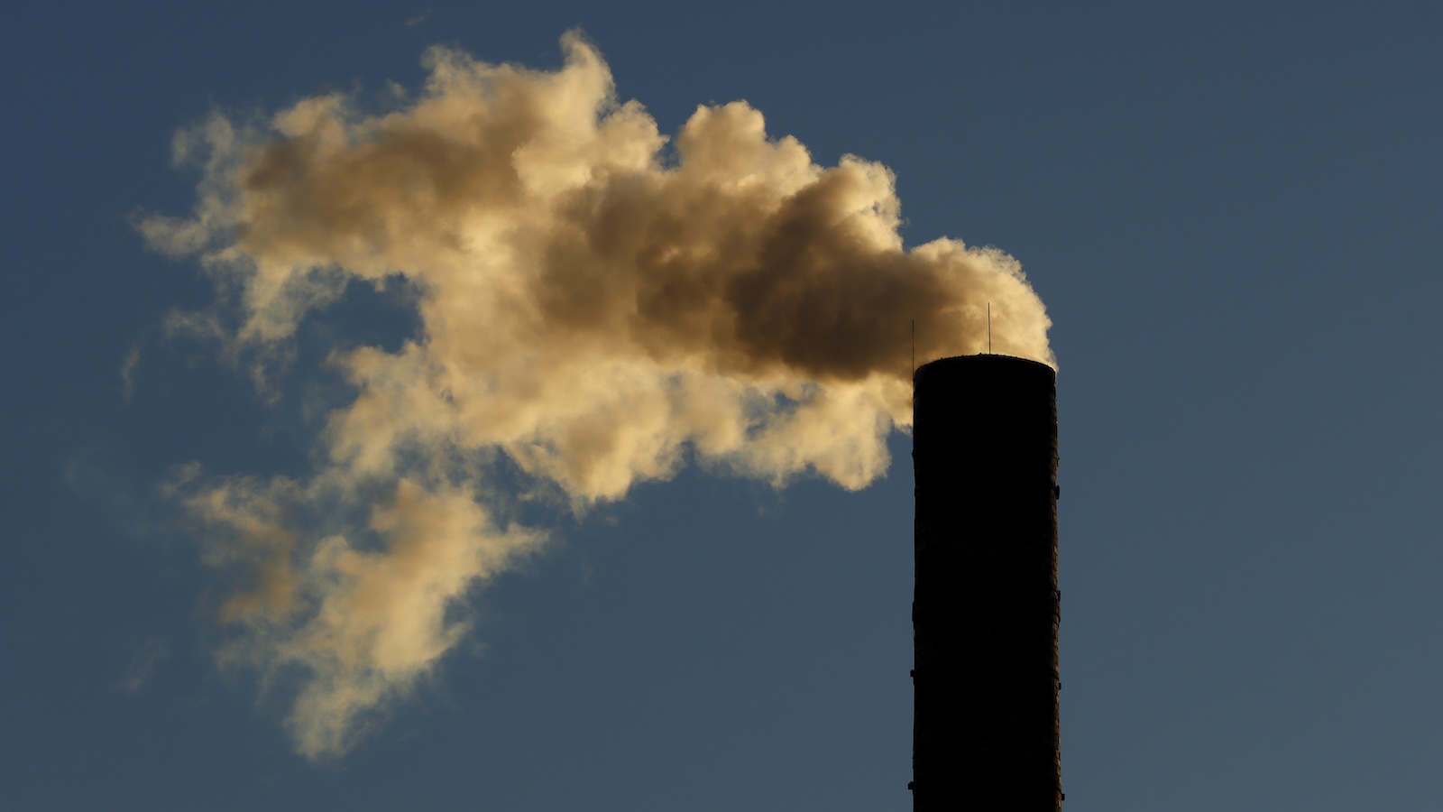 A smokestack spews emissions against a blue sky