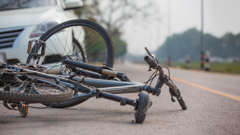 A mangled bicycle sitting on the road in front of a white sedan after an accident