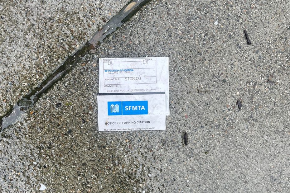 A parking citation issued by the SFMTA lies on a wet concrete sidewalk in Bayview.