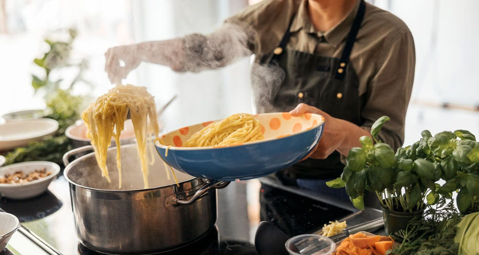 A person strains cooked spaghetti out of a steaming pot on an induction range into a serving bowl.