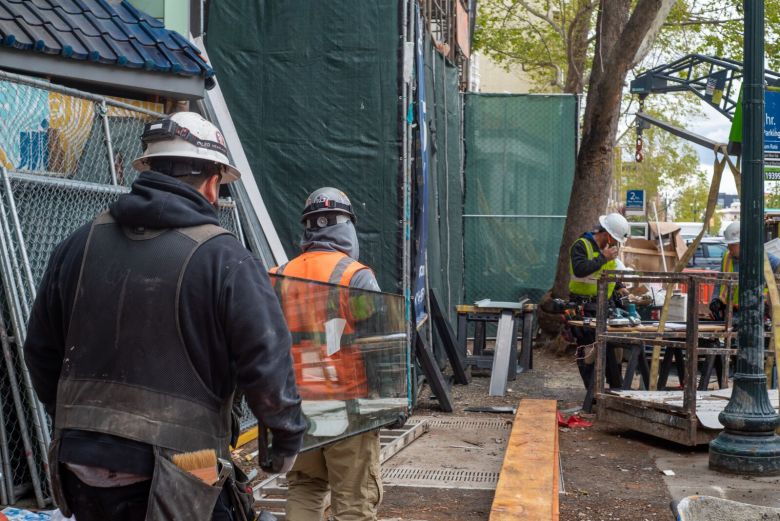 Construction workers haul a pane of glass at a worksite