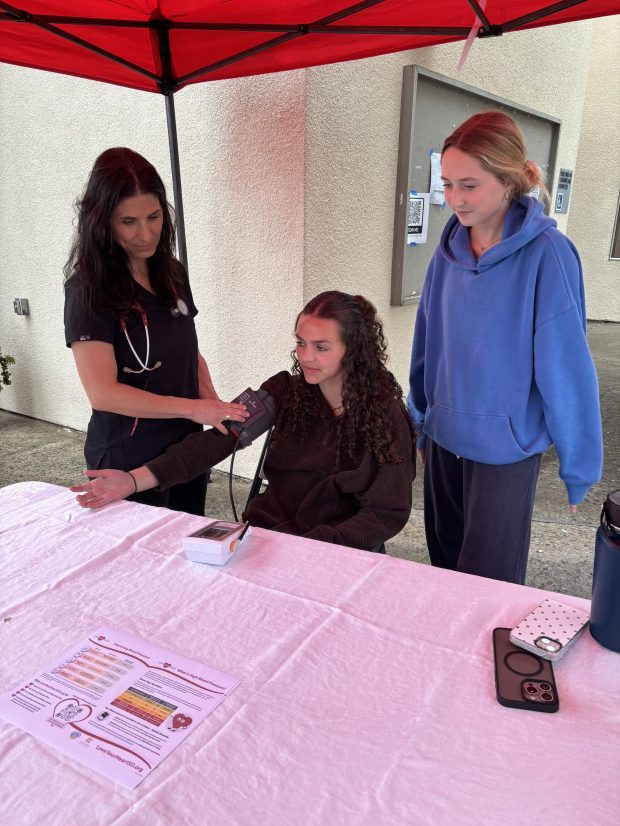 Charley Williams (in blue sweatshirt) watches as Gabrielle Hill takes Maia Poch's blood pressure reading during a recent screening event at La Jolla High School. (Dana Williams)