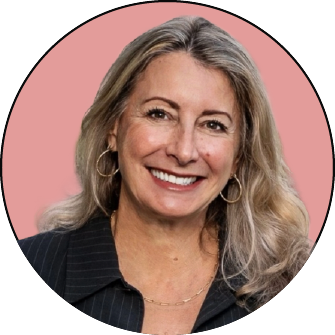 Smiling woman with long blonde hair wearing hoop earrings and a dark pinstripe blazer, posed in front of a pink background.