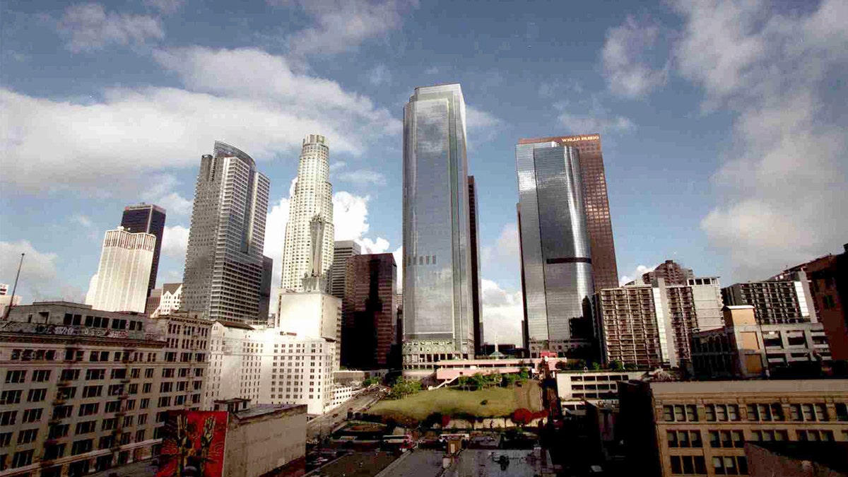 Sunlight breaks through clouds, illuminating downtown skyscrapers and surrounding hills after a rainstorm.