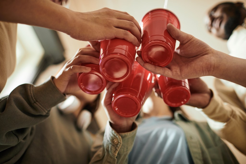 Low angle view of a group of teenagers toasting with red plastic cups at a party.