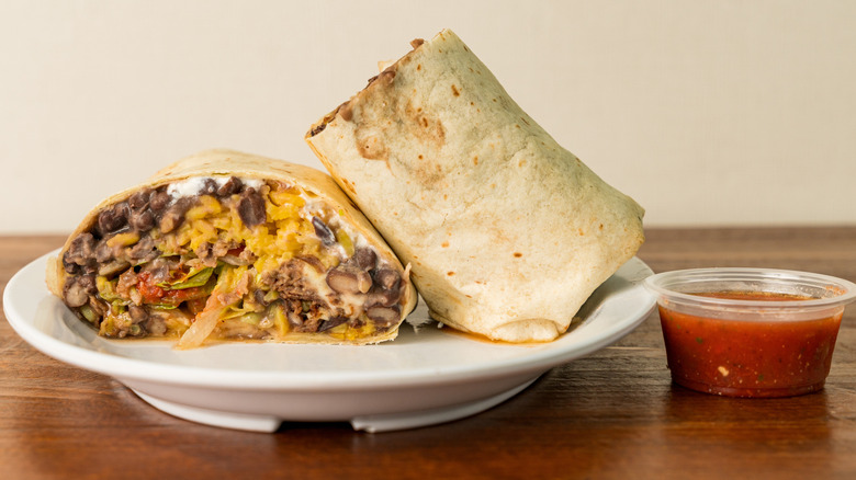 Bean, cheese, meat burrito cut in half with small plastic container of salsa