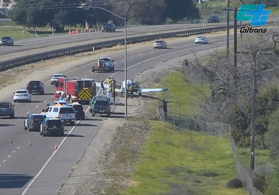 Emergency landing of a plane on a highway shoulder, surrounded by emergency vehicles.