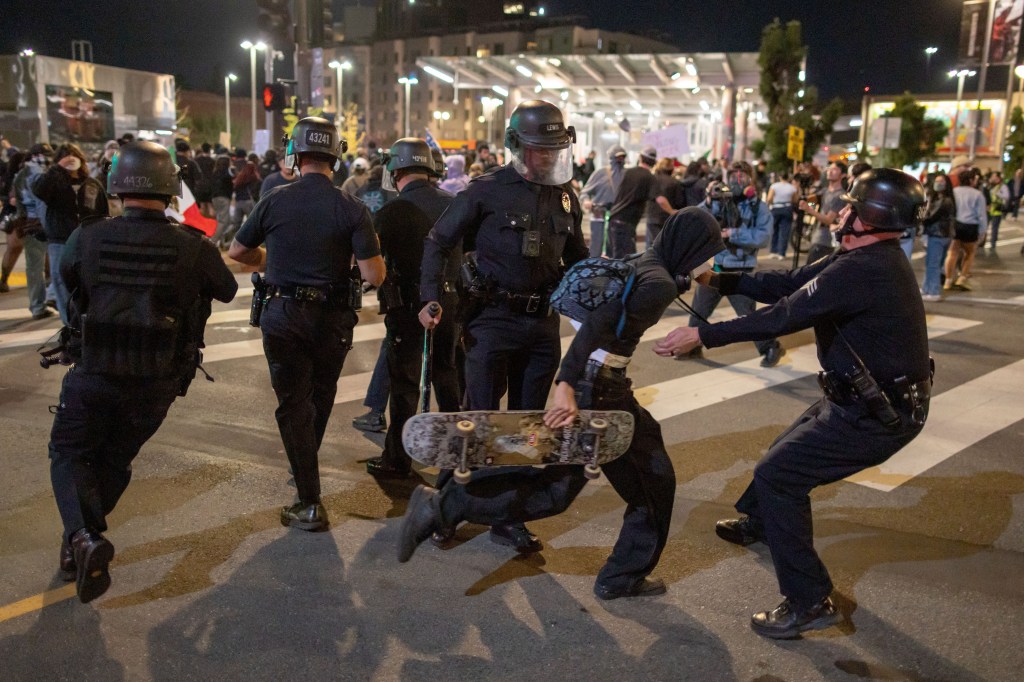 Police officers detain a person holding a skateboard during a protest in Los Angeles.