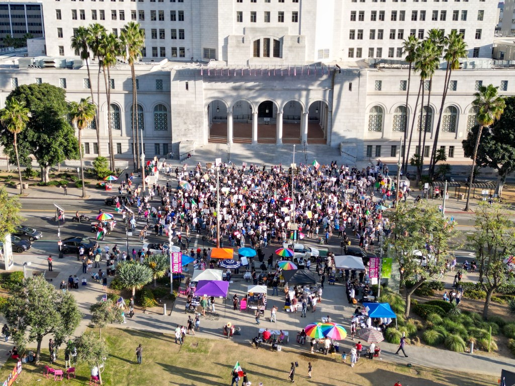 Protest against ICE in downtown Los Angeles with a crowd gathered in front of a large building.