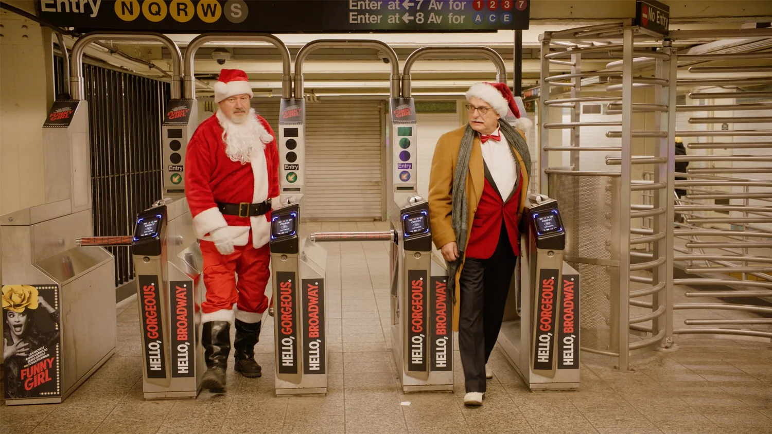 Two men, one dressed as Santa and one in a tan jacket with a Santa hat, stand next to turnstiles in a subway station. A "Funny Girl" poster is visible on the left.