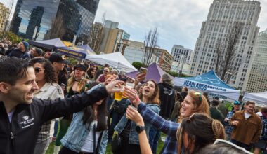 People gathered in a circle, standing outside and raising their glasses as they cheers with beer.