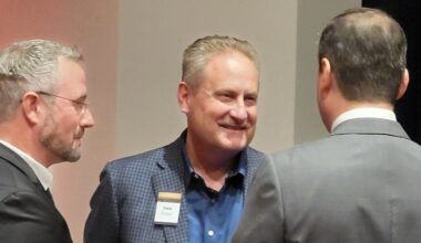 three men speaking, one with their back to the camera, the other in profile