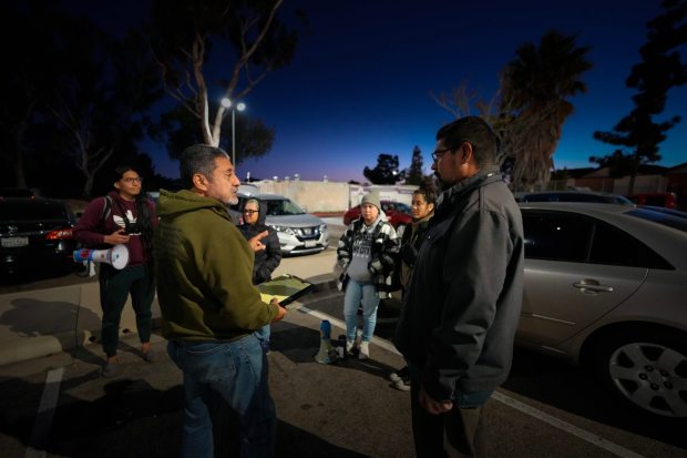 On Wednesday, Feb. 4, 2026, a team of volunteers meets before sunrise in Linda Vista. Rommel D., left, and Benjamin Prado, right, divide the volunteers into smaller teams before heading out on community patrols looking for federal agents.  (Nelvin C. Cepeda / The San Diego Union-Tribune)