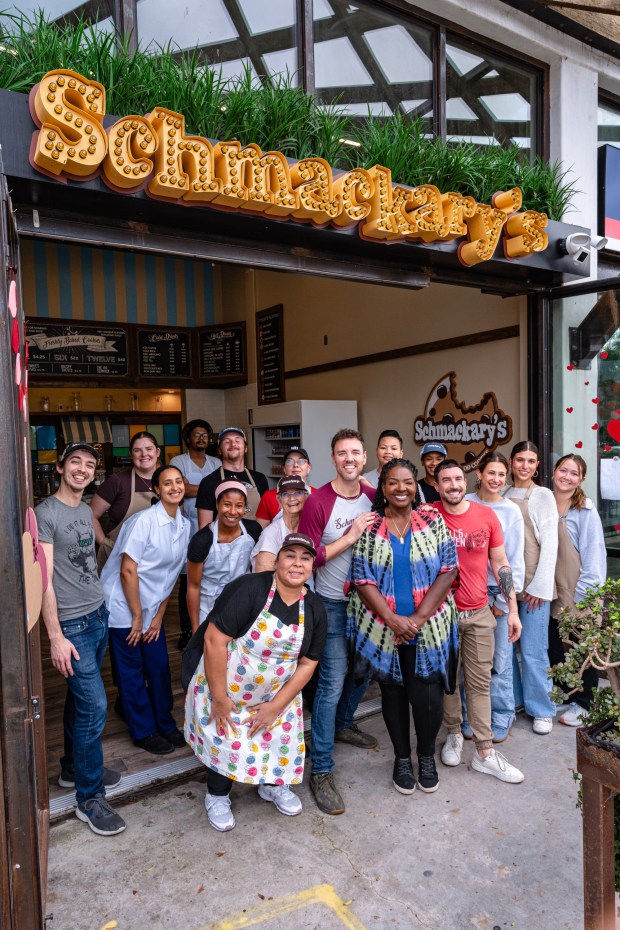Sharian Lott, center foreground, is the franchise owner for the first West Coast location of Schmackary's cookies, opening Feb. 28, 2026, in San Diego's Hillcrest. Lott is flanked by Schmackary's founder Zachary Schmal, left, and chief operating officer Jonny Polizzi, along with the new shop's employees. (Jeromy Estabillo Chan/Slique Media)