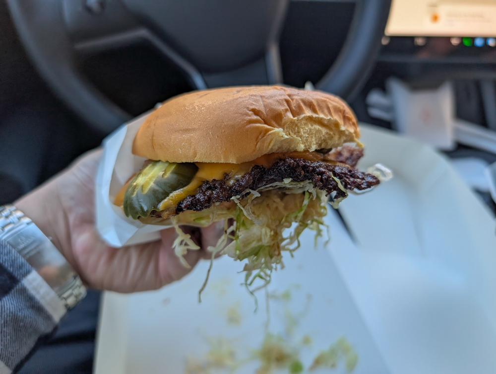 A hand holds up a smash burger in the car.