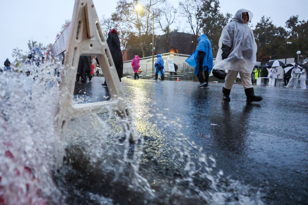 Water floods down a gutter as parade attendees wearing ponchos walk up Colorado Blvd in the rain before the start of the 137th Rose Parade.