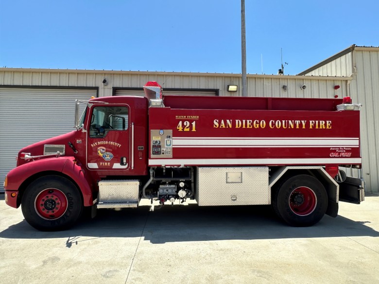 A small red fire truck with the words "San Diego County Fire" painted on the side, parked in front of an outdoor garage.