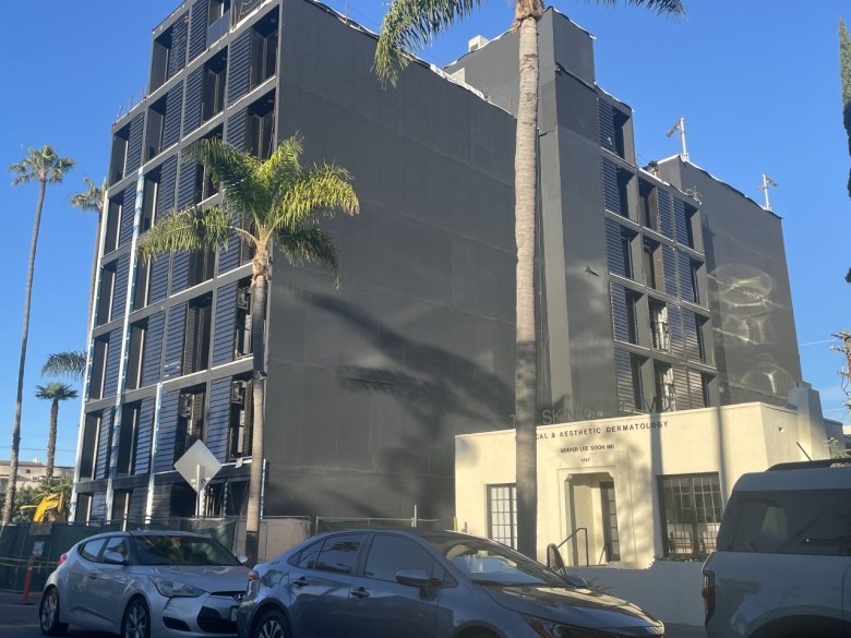 A beam of sunlight is cast on a new building with a construction fence around the street-level perimeter. It's a factory-built structure intended to become housing.