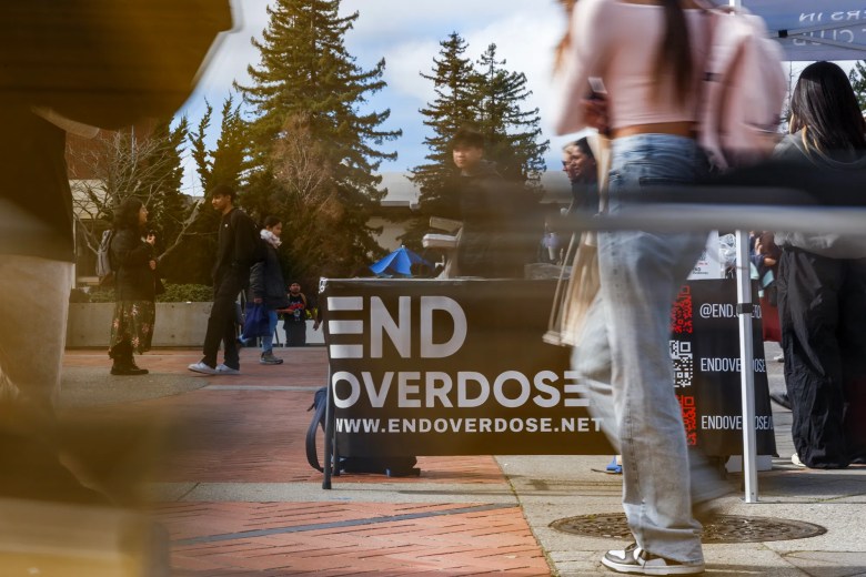 People walk past a table that reads "end overdose" on a busy college quad