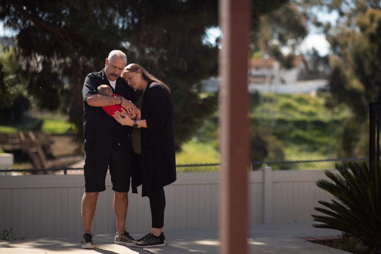 A foster couple holds a small baby and stares lovingly at it.