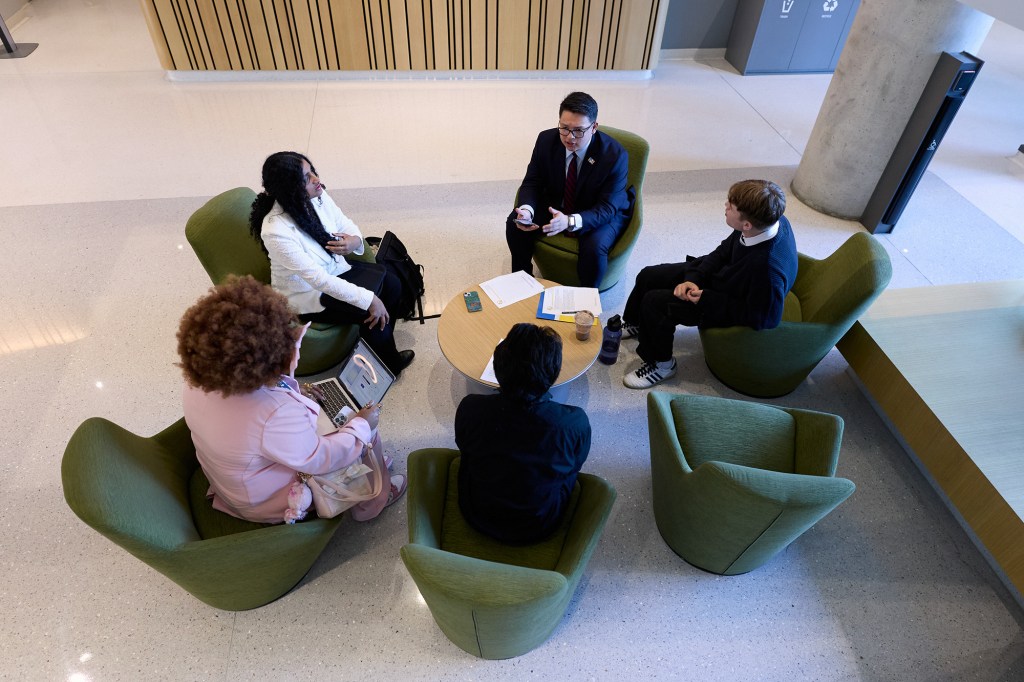 An overhead view of five people sitting in green chairs arranged in a circle as they talk to each other.