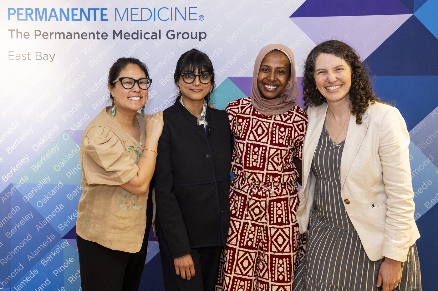 Four attendees pose together in front of a Permanente Medicine Group East Bay banner at the Global Health Consortium.
