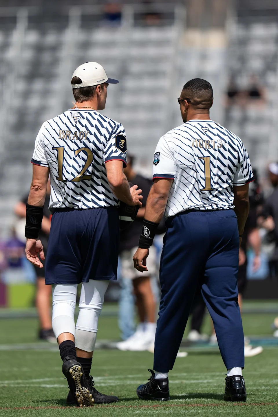 Founders quarterbacks Tom Brady (12) and Jalen Hurts (1) walk on the field during warmups ahead of the Fanatics Flag Football event, March 21, 2026, in Los Angeles.