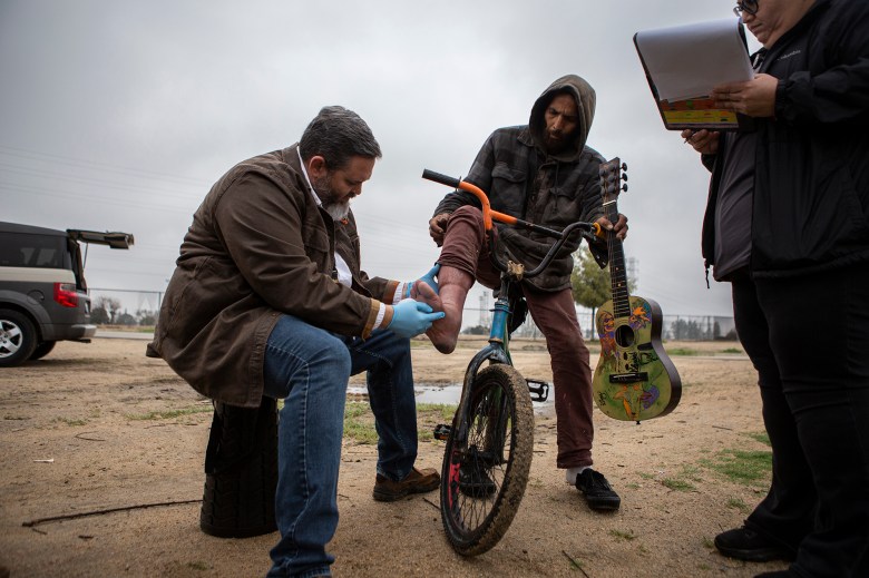 Dr. Mathew Beare examines a patients foot at a meeting area near the Kern River on March 16, 2023. Photo by Larry Valenzuela, CalMatters/CatchLight Local
