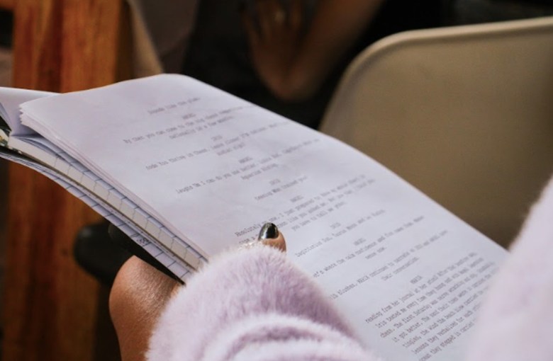 A closeup of a script page held by a hand with painted nails -- the person's pink sweater can be seen.