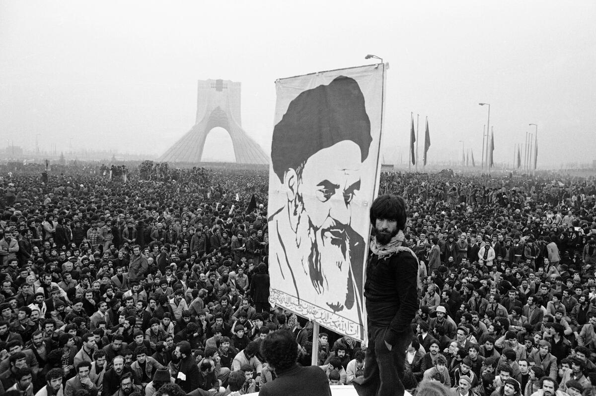 People in a massive crowd hold up a large poster of a man with a beard and dark turban