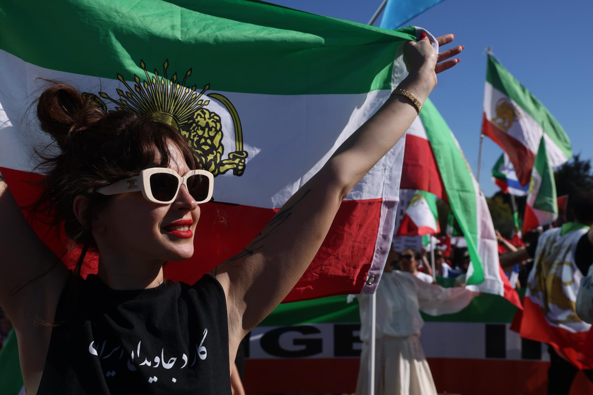 A woman in sunglasses smiles and holds an Iranian flag.