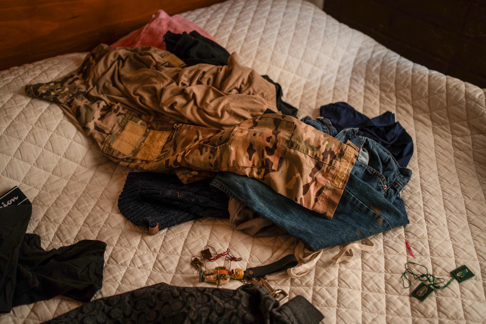Camouflage clothing and personal belongings lie on an unmade bed