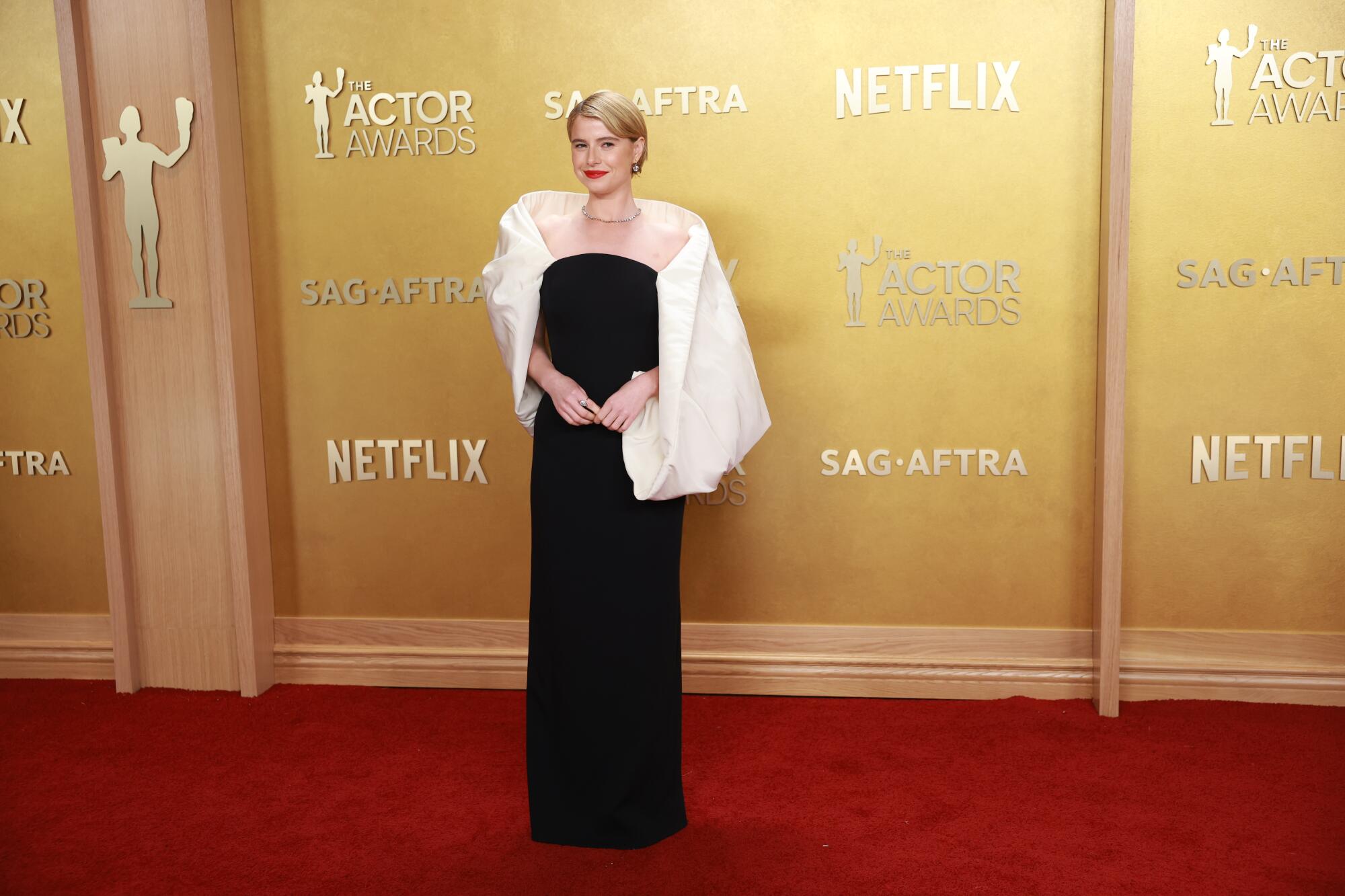 Jessie Buckley, wearing a black gown with a white shawl, poses on the red carpet. 