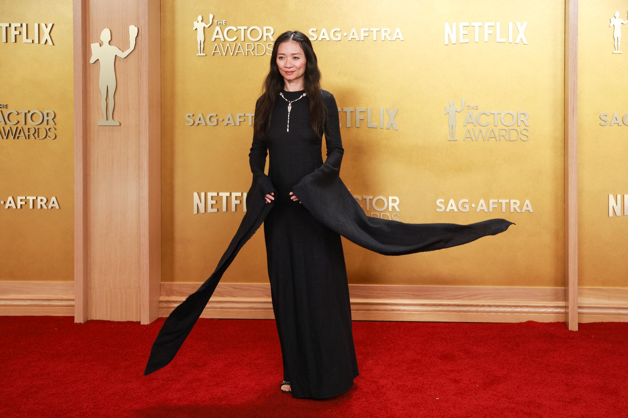 Chloé Zhao, wearing a black gown, poses on the red carpet. 