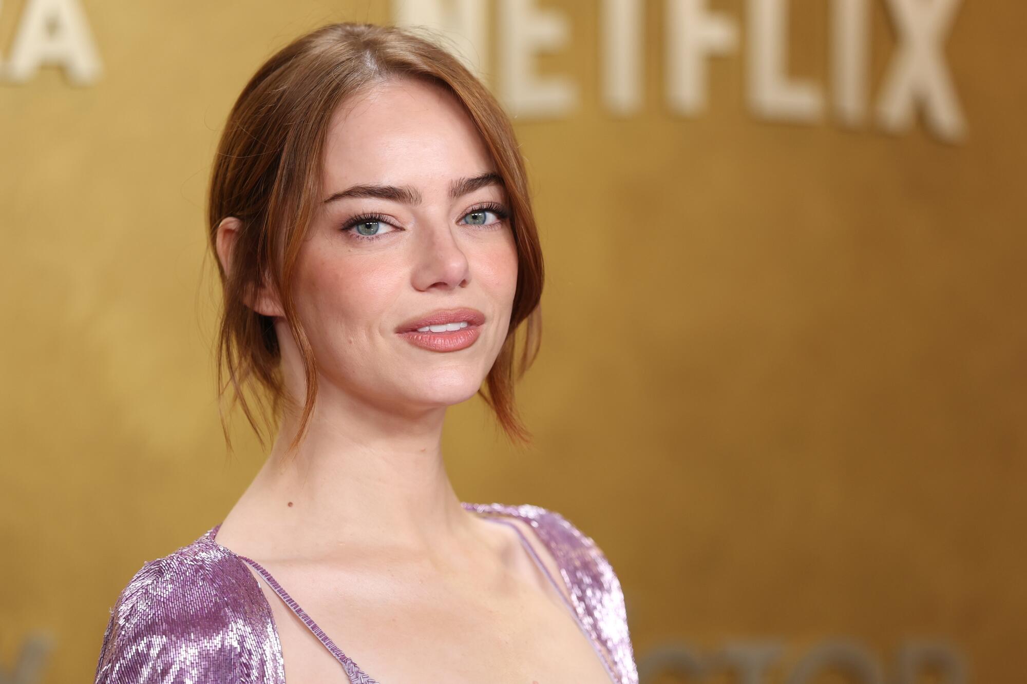 Emma Stone, wearing a purple dress, smiles on the red carpet. 