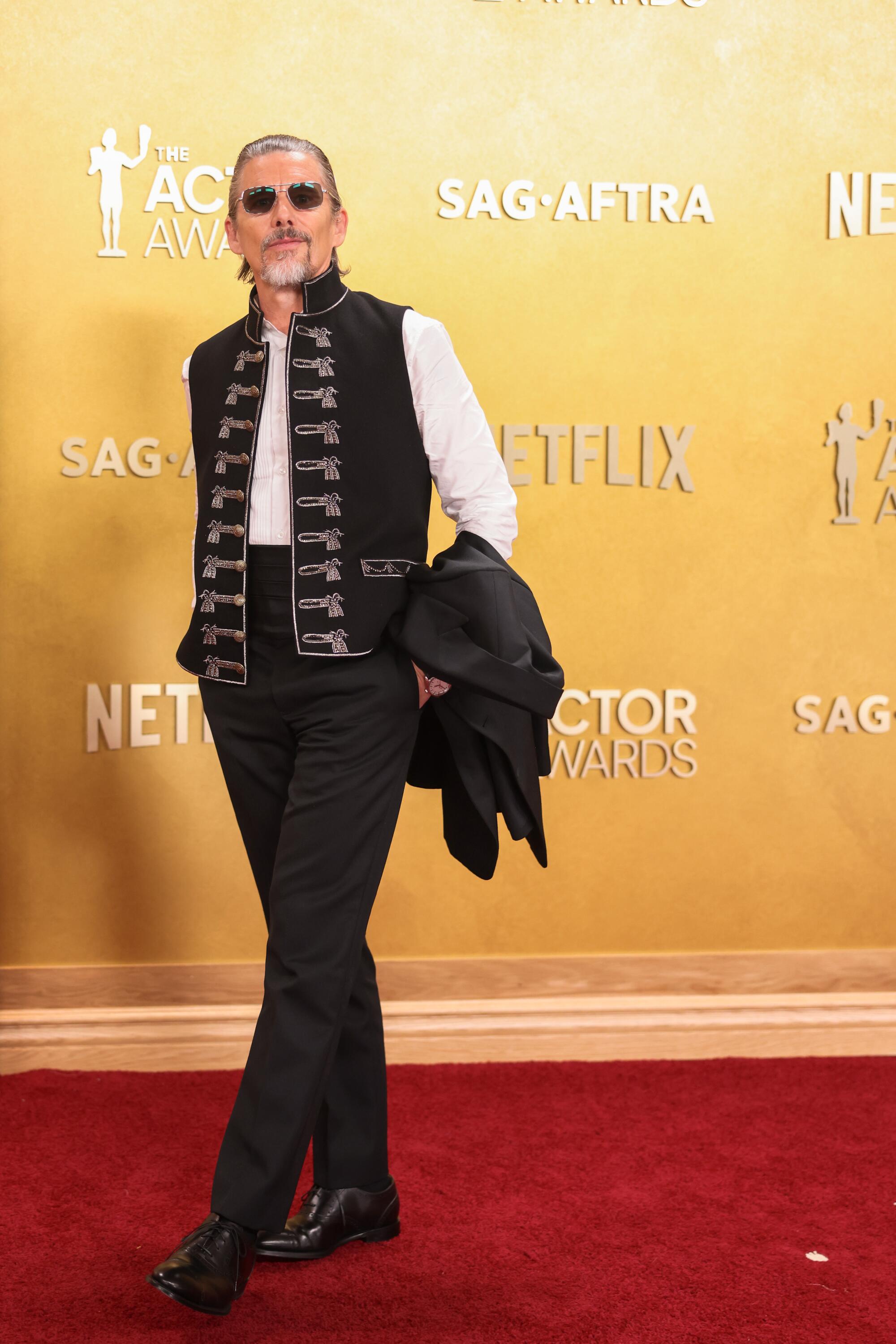 Ethan Hawke, wearing a military-type vest, poses on the red carpet. 