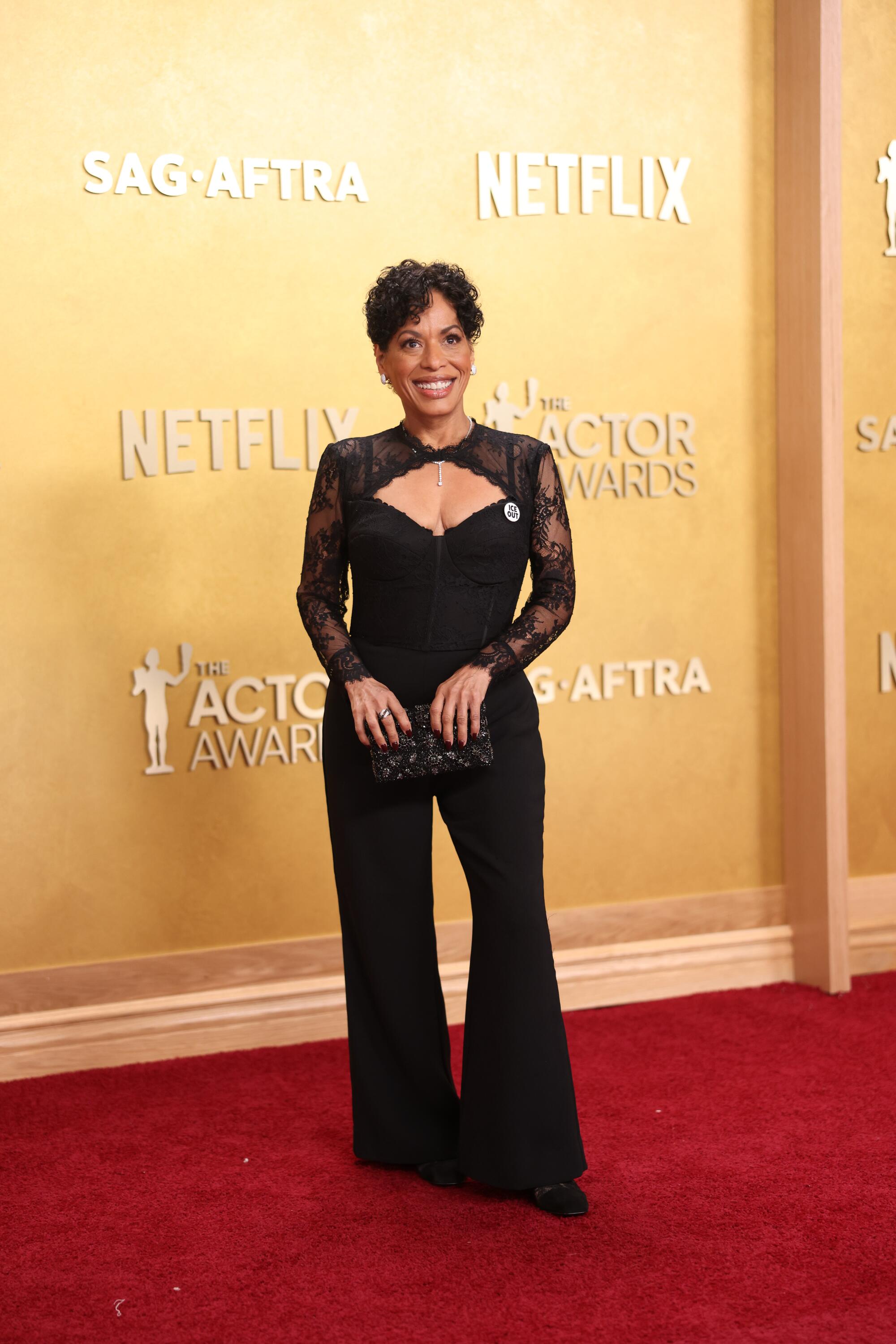Liza Colon-Zayas, wearing a black lace jumpsuit, poses on the red carpet. 